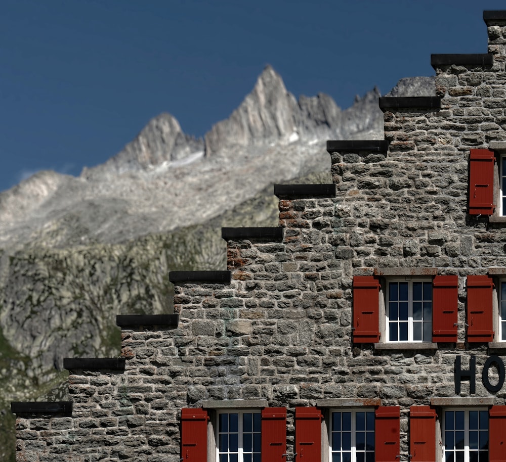 a stone building with red shutters and a mountain in the background