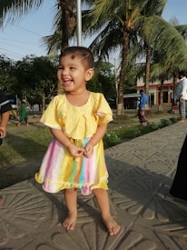 A smiling toddler wearing comfortable, colorful clothing in a natural outdoor environment.