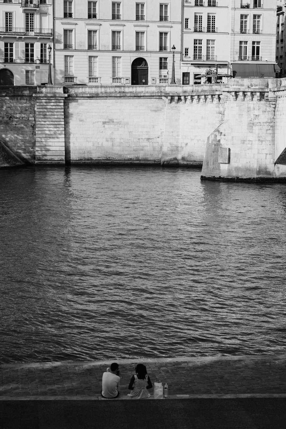 three people sitting on the edge of a body of water