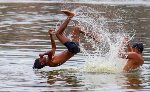 Two people are joyfully playing in the water, with one person mid-flip and another splashing water, creating a dynamic scene full of movement and excitement.