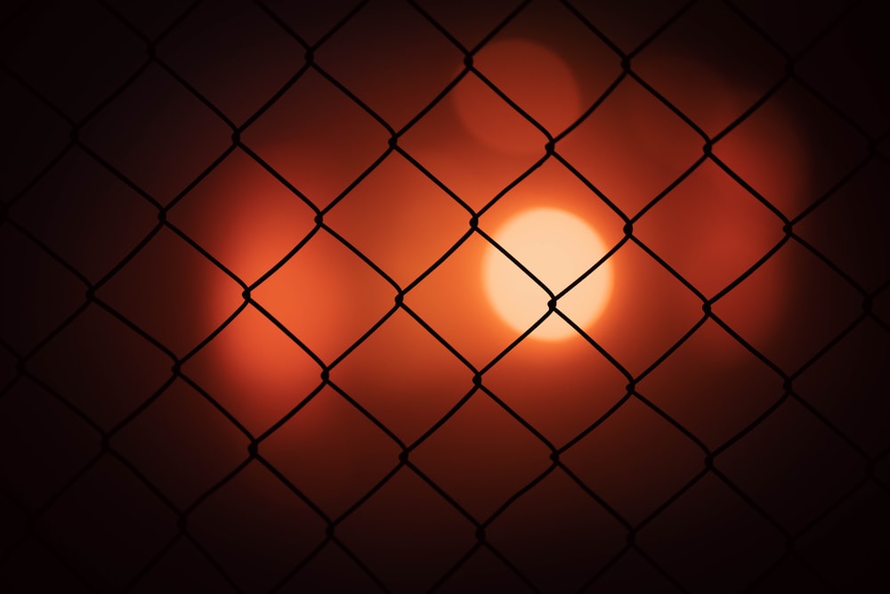 the sun is setting behind a chain link fence