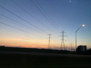 Wide shot of electrical transformers and power lines at dusk with deep blue sky.