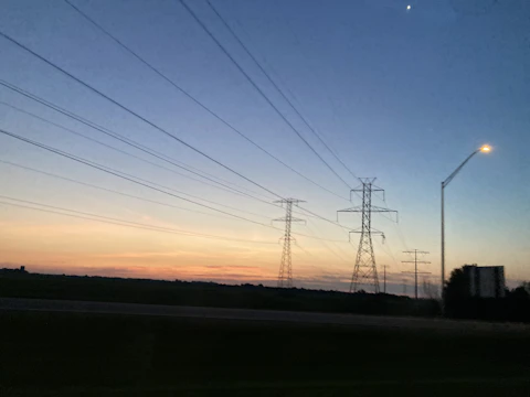Wide shot of electrical transformers and power lines at dusk with deep blue sky.