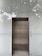 An elevator with metallic doors is set into a modern exterior with frosted glass panels. The reflection of surrounding trees and a building is faintly visible on the glass, giving a somewhat ethereal appearance.
