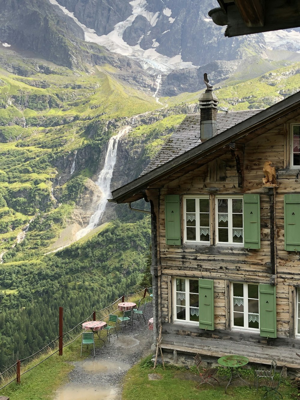 a wooden house with green shutters and a waterfall in the background