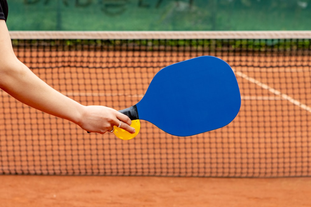 a person holding a ping pong paddle on a tennis court