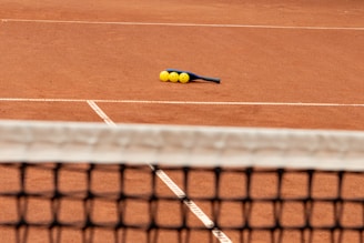 Close-up of tennis rackets and balls resting on a clay court surface.