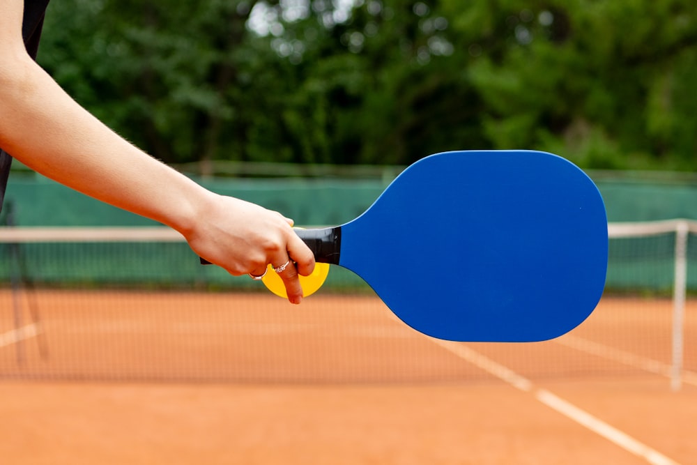 a person holding a ping pong paddle on a tennis court