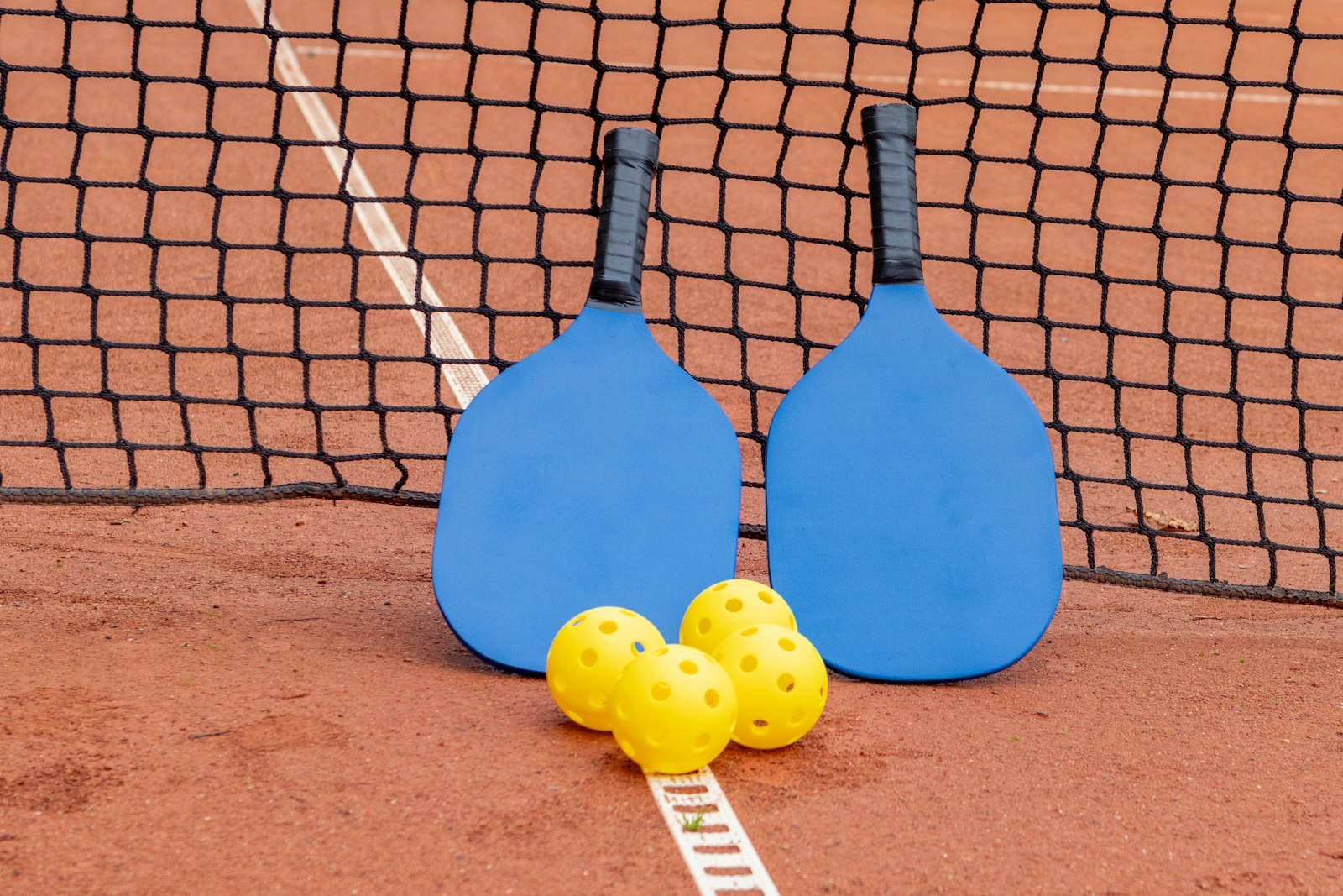 Two pickleball paddles and three balls on an outdoor court