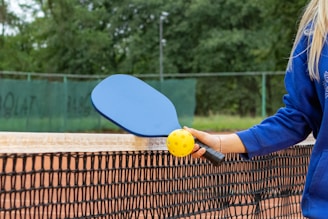 A cheerful cartoon paddle ball character holding a paddle on a bright court background.