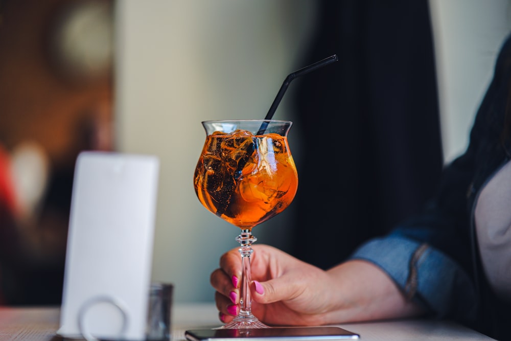 a woman is holding a glass with a drink in it