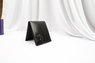 A sleek black leather wallet resting on a white marble surface with gold accents.