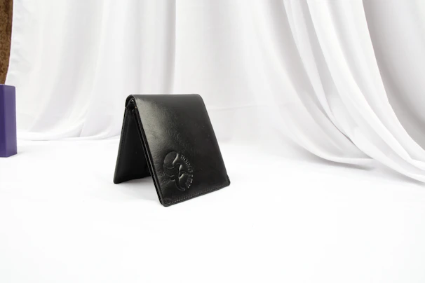 Matte black leather wallet resting on a soft cream fabric with subtle gold highlights