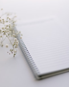 a notebook with a pen and a flower on a table