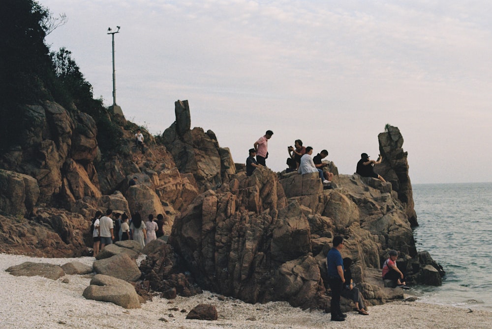 a group of people standing on top of rocks near the ocean