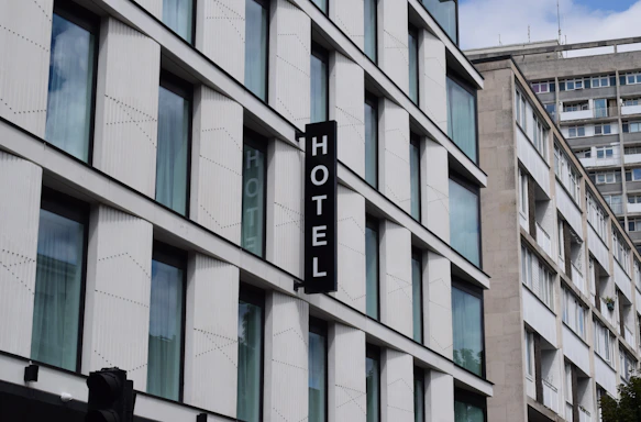 A modern building with multiple large glass windows arranged in a grid pattern. A vertical sign with the word 'HOTEL' is attached to the facade. The architecture is clean and minimalistic, with a focus on straight lines and uniformity.