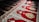 Intricate red carpet with elaborate patterns, including floral and geometric designs. The carpet is divided into sections, each featuring a central motif surrounded by detailed border elements. Sunlight casts shadows across parts of the carpet, enhancing the texture and depth of the design.