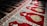 Intricate red carpet with elaborate patterns, including floral and geometric designs. The carpet is divided into sections, each featuring a central motif surrounded by detailed border elements. Sunlight casts shadows across parts of the carpet, enhancing the texture and depth of the design.