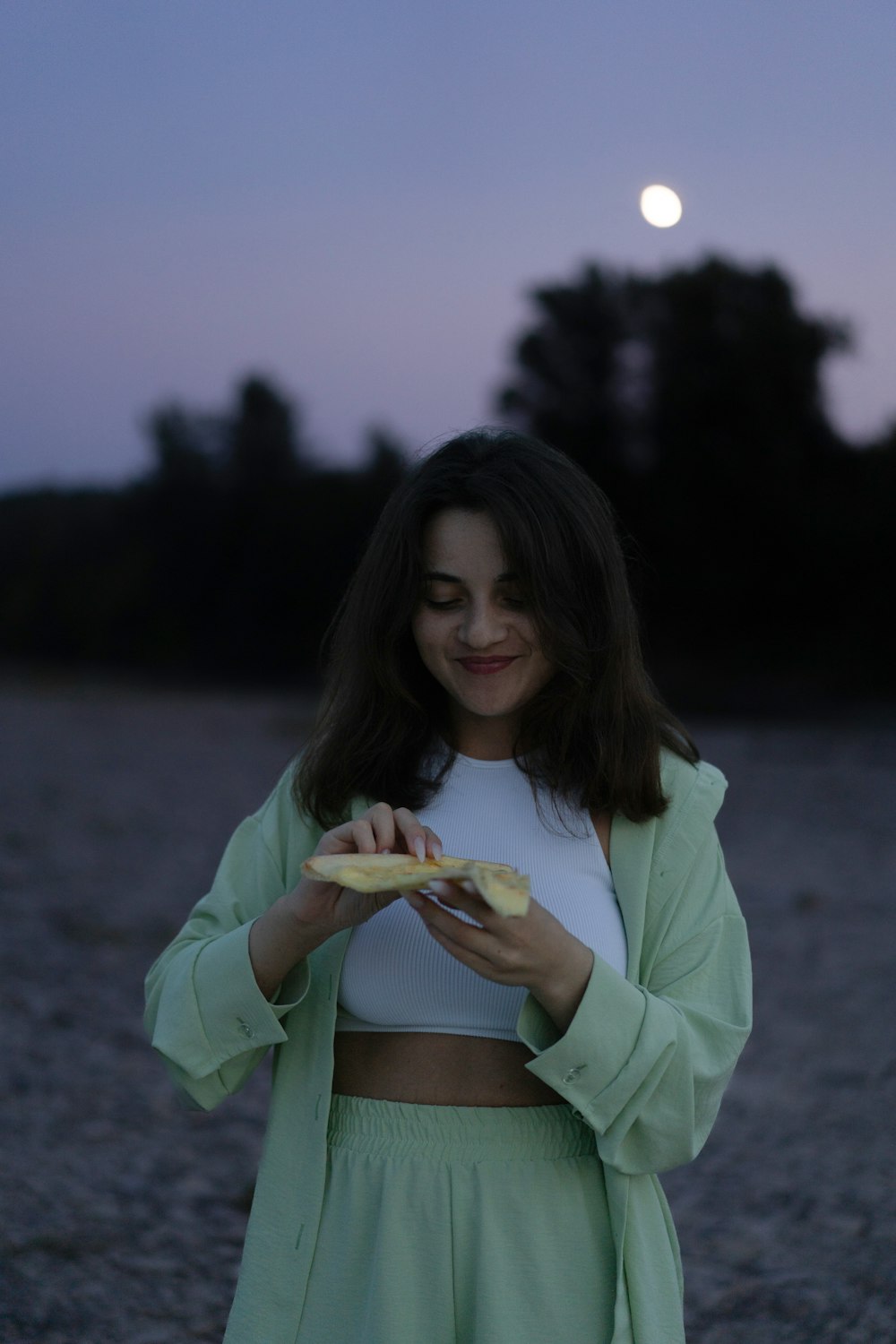 a woman standing on a gravel road eating a hot dog