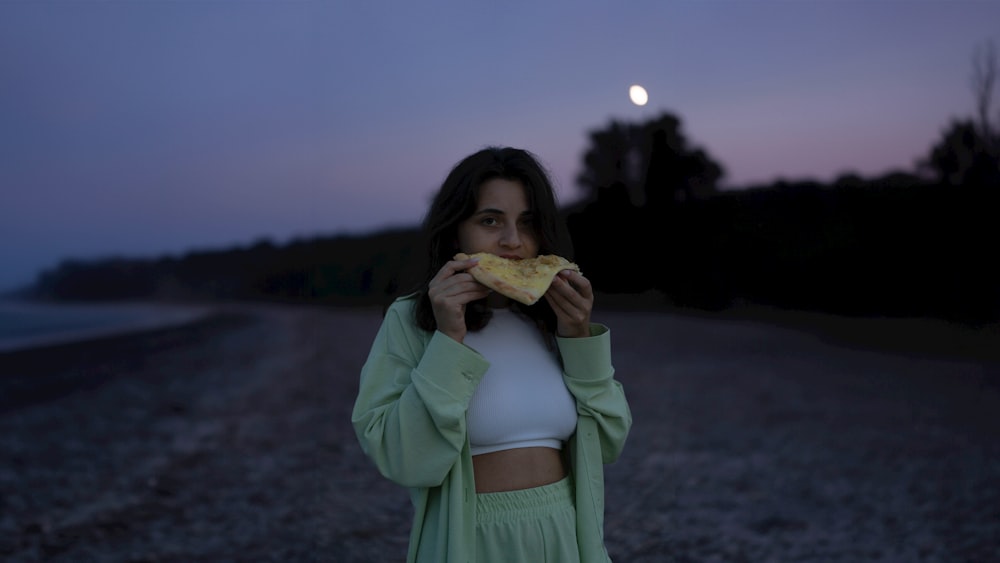 a woman eating a slice of pizza on a gravel road