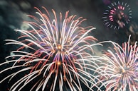 Brightly colored fireworks bursting in the night sky, with trails of vibrant red, white, and blue light creating intricate patterns against a dark background.