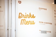A section of a drinks menu with categories such as 'Coffee', 'Non-Coffee', and 'Fruit Juice'. The word 'Sold Out' is written on a piece of paper next to one of the items. The menu features headings in bold, uppercase letters in a warm, brownish color.