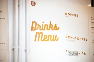 A section of a drinks menu with categories such as 'Coffee', 'Non-Coffee', and 'Fruit Juice'. The word 'Sold Out' is written on a piece of paper next to one of the items. The menu features headings in bold, uppercase letters in a warm, brownish color.