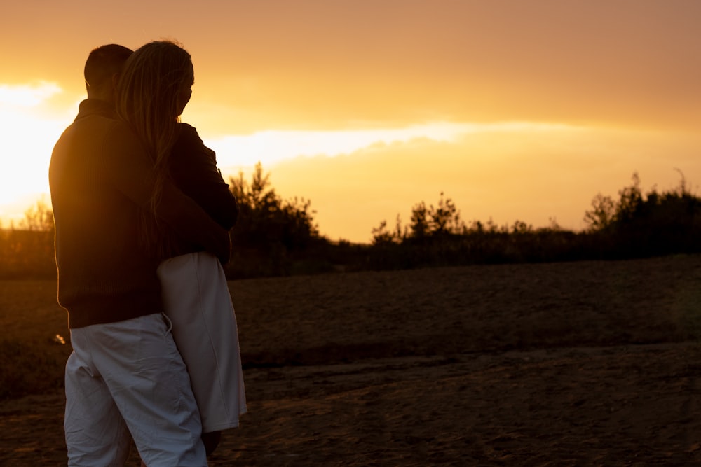 a man and a woman standing in a field at sunset