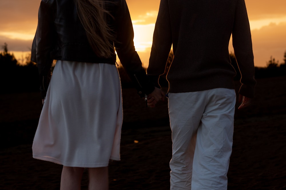 a man and a woman hold hands as the sun sets