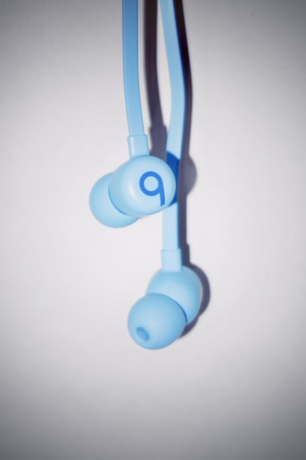 A pair of light blue in-ear headphones with a minimalistic design and the letter 'b' prominently displayed on each earpiece. The headphones are shown against a plain white background, with shadows adding depth.