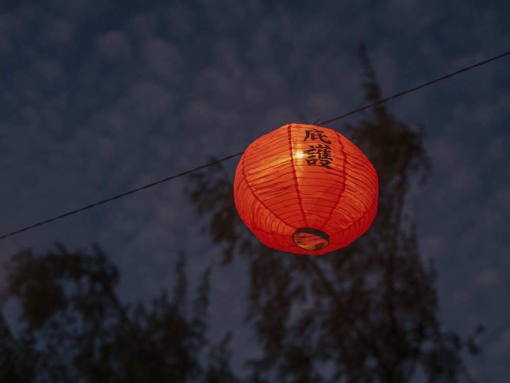 a red lantern hanging from a wire with trees in the background