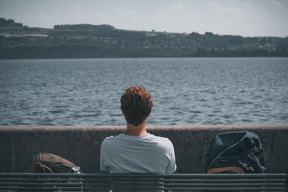 a person sitting on a bench next to a body of water