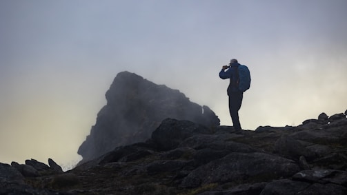 Wide shot of a professional explorer examining equipment near a misty, expansive natural landscape at dawn.