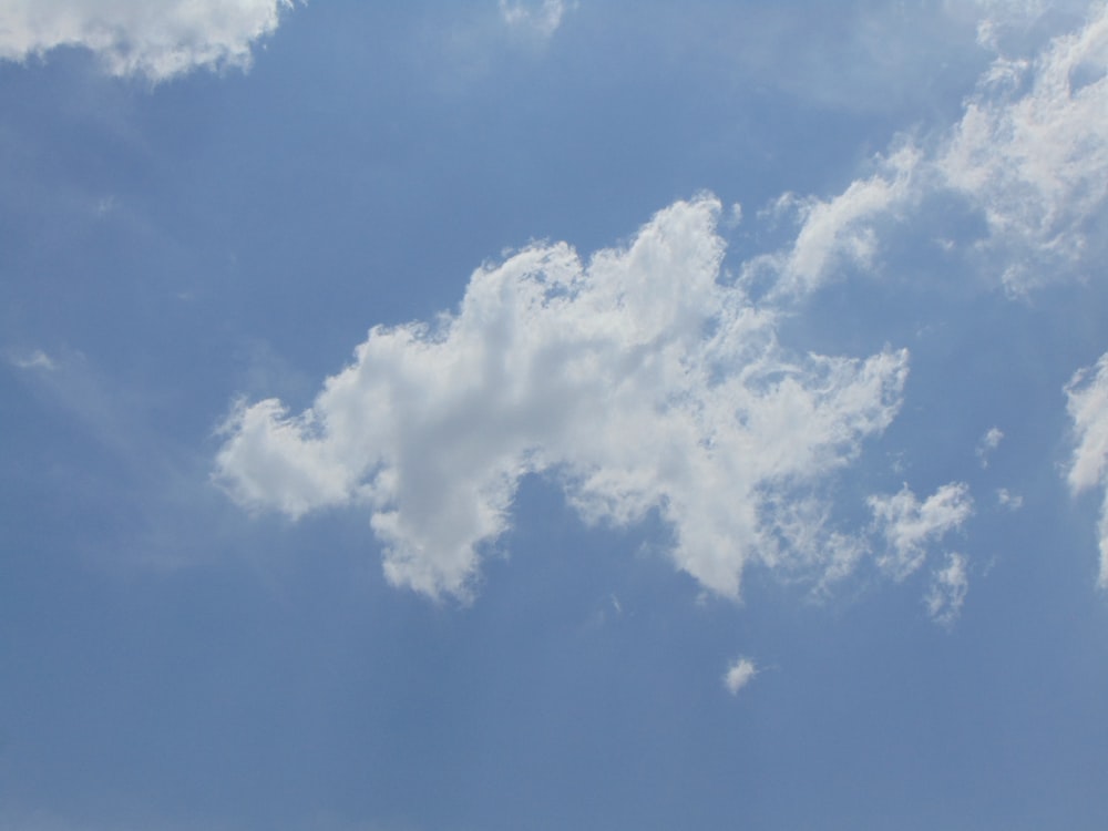 a plane flying through a blue sky with white clouds