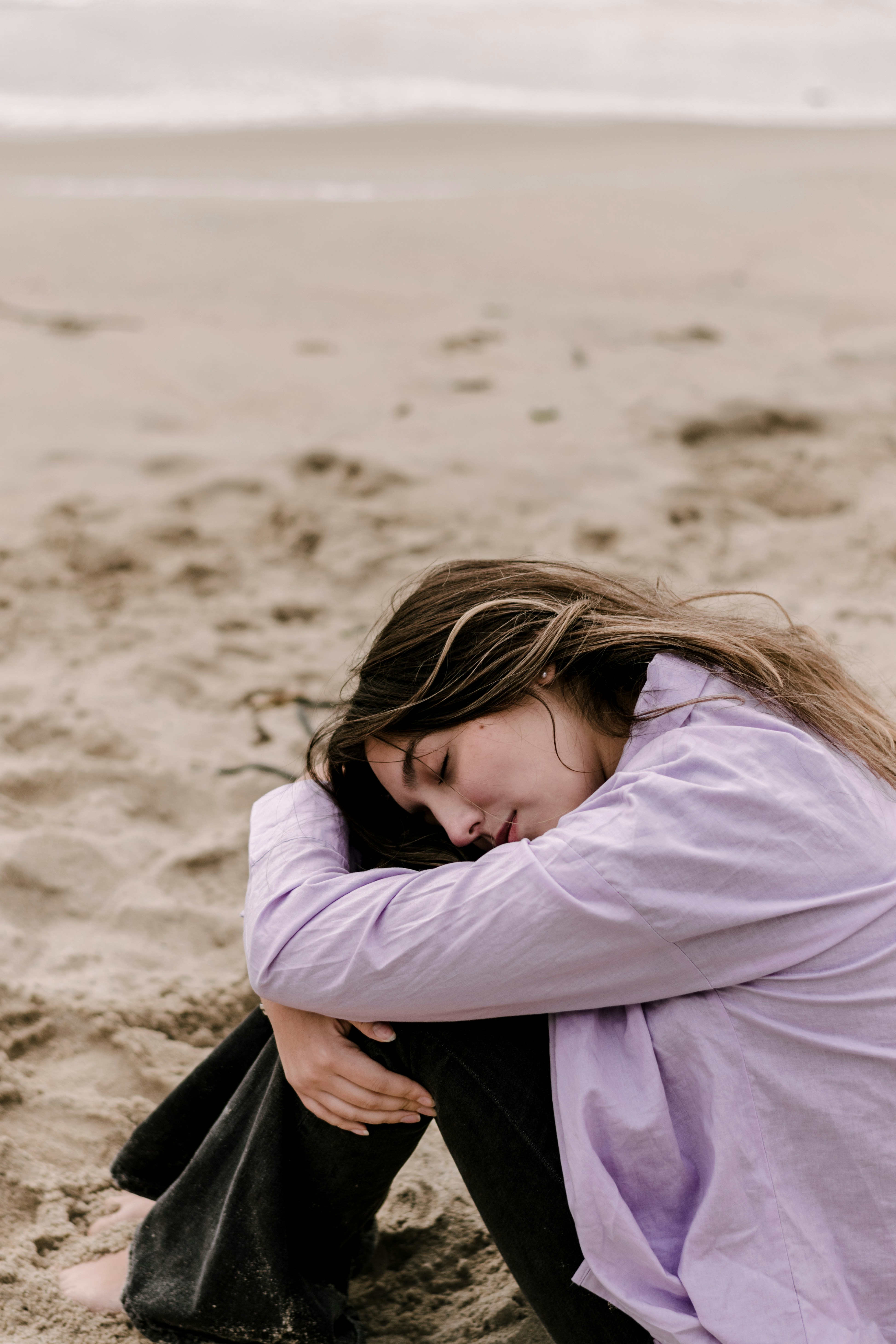 a woman sitting on the beach with her head in her hands