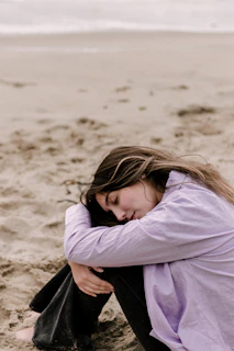 a woman sitting on the beach with her head in her hands