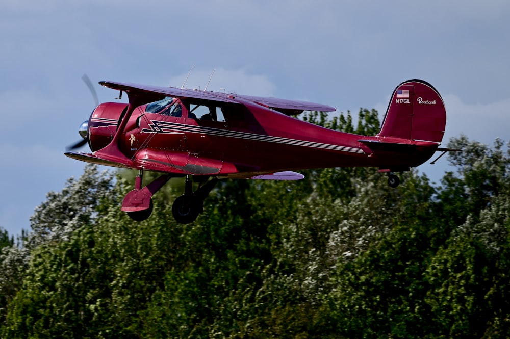 a small red airplane flying over a forest