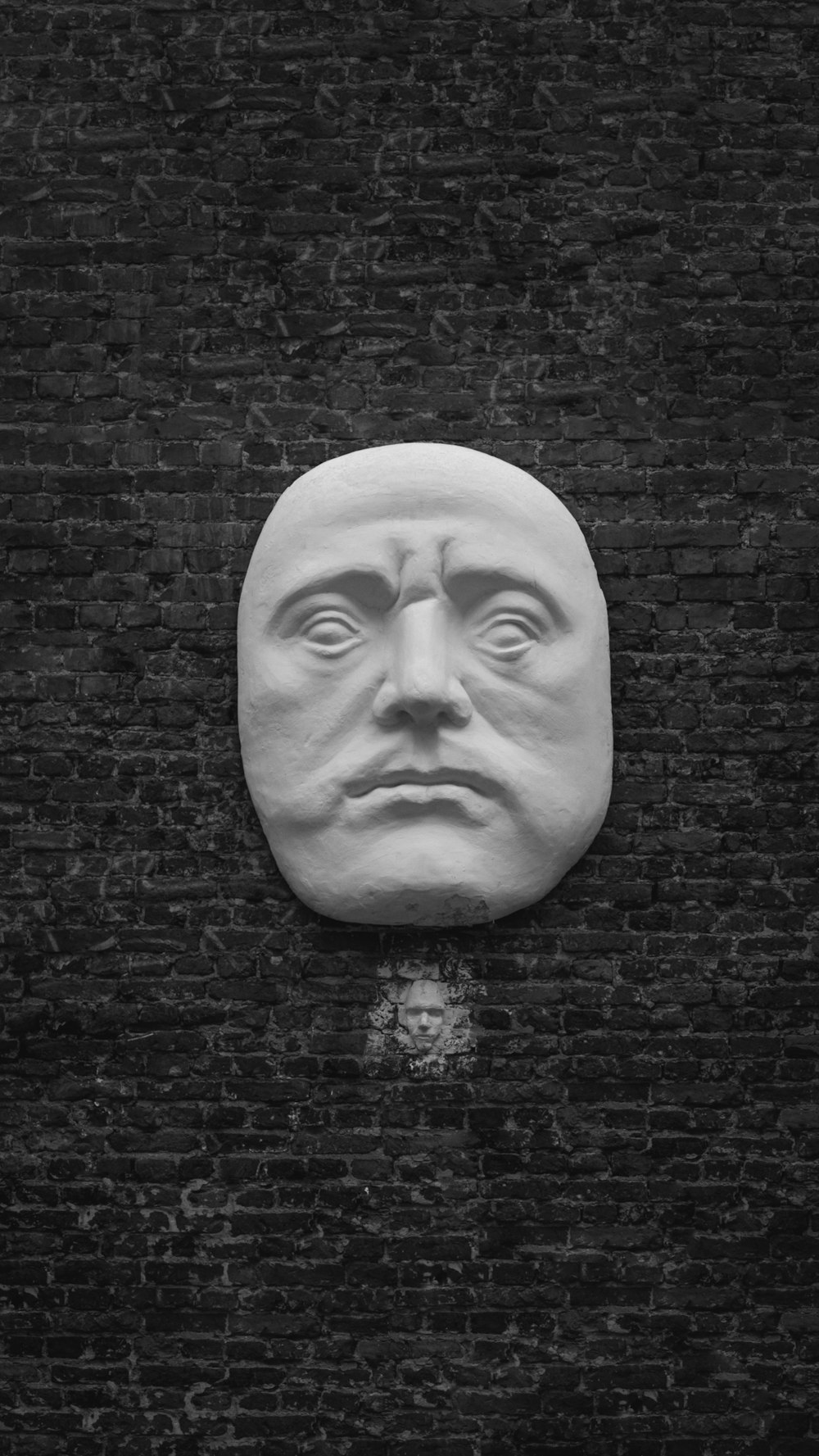 a black and white photo of a face on a brick wall