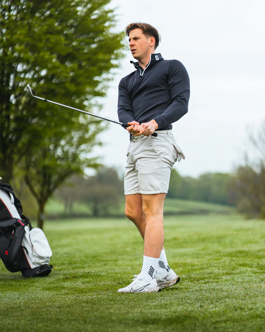 A friendly golfer smiling on a sunny course, holding a club with a scenic fairway in the background