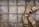 Several pairs of beige sandals with small holes are resting on a textured surface. The ground is covered with a light dusting of white snow, creating an interesting contrast with the deeper earth tones of the tiles.