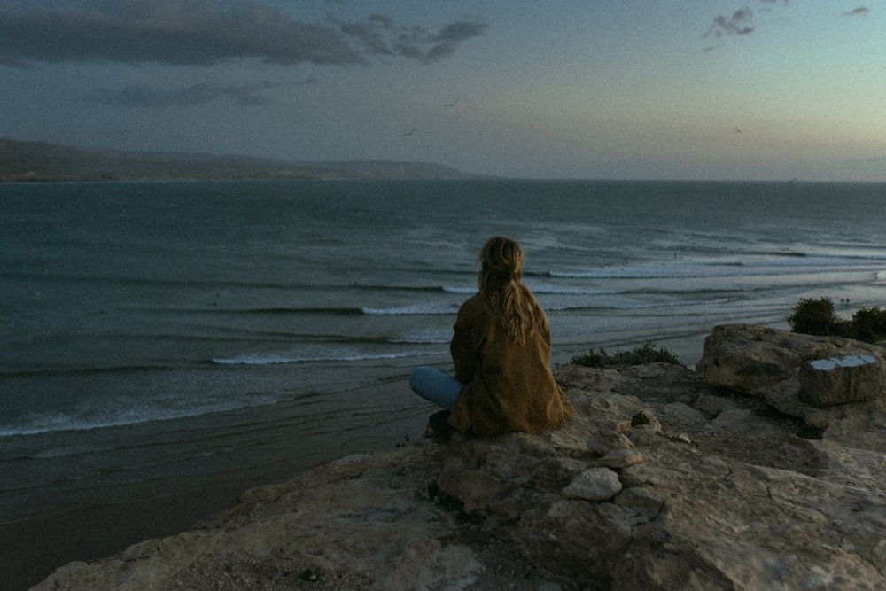 a person sitting on a rock looking out at the ocean