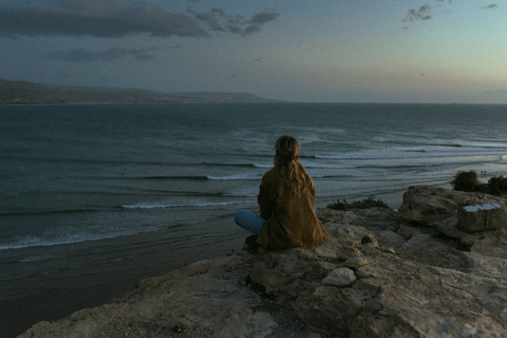 uma pessoa sentada em uma rocha olhando para o oceano