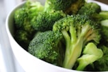 A close-up view of fresh green broccoli florets in a white bowl, with detailed textures visible on the surfaces.