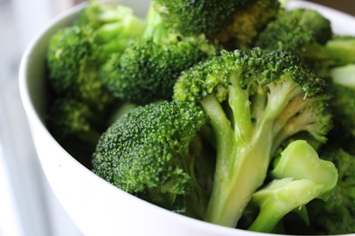 A close-up view of fresh green broccoli florets in a white bowl, with detailed textures visible on the surfaces.
