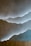 A textured wall with a layered design resembling mountains, highlighted by soft lighting from behind the layers. At the bottom, there is a wooden plank or surface, creating a contrast with the smooth plaster-like texture of the wall.