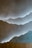 A textured wall with a layered design resembling mountains, highlighted by soft lighting from behind the layers. At the bottom, there is a wooden plank or surface, creating a contrast with the smooth plaster-like texture of the wall.