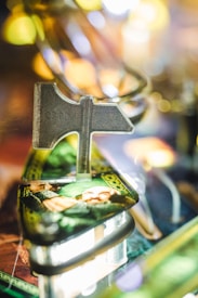 A close-up view of a pinball machine featuring a metal detail shaped like a directional sign, with vivid artwork beneath it. The background is blurred with bright lights, creating a vibrant, colorful atmosphere.