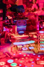 A vibrant and colorful pinball machine with illuminated buttons and detailed patterns. The text 'THE MOST SECRET MACHINE' is visible on a metallic surface.