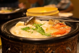 A steaming bowl of ajiaco soup garnished with corn, chicken, and herbs in a traditional clay pot