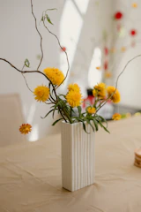 A close-up of a textured stoneware vase in cheerful yellow, holding fresh wildflowers.